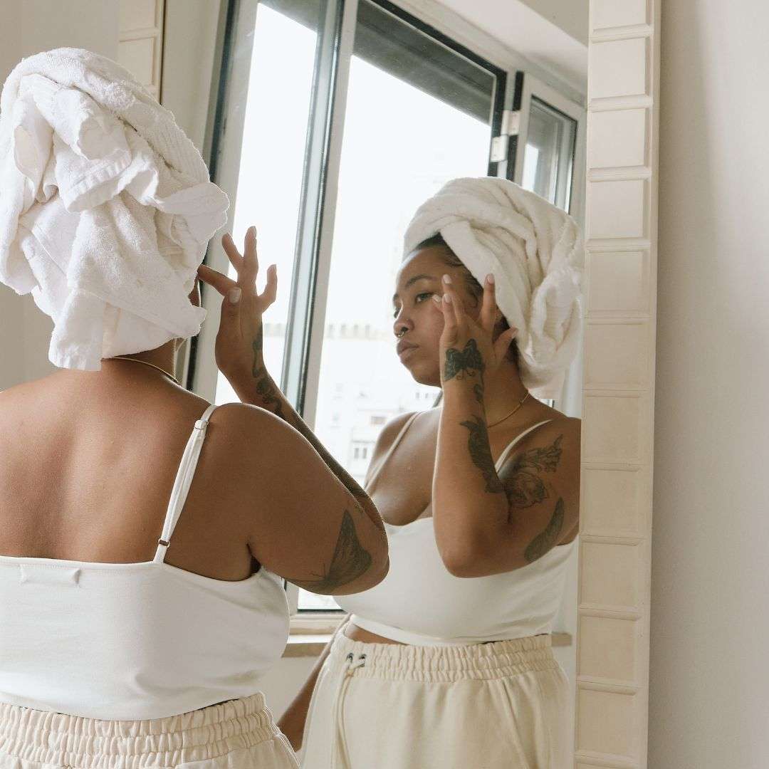 black woman looking in mirror after shower and touching her cheek