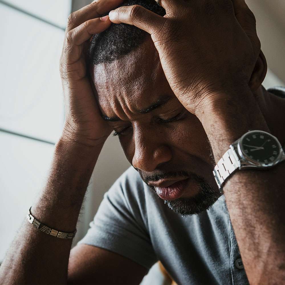 black man holding his head with closed eyes looking distressed